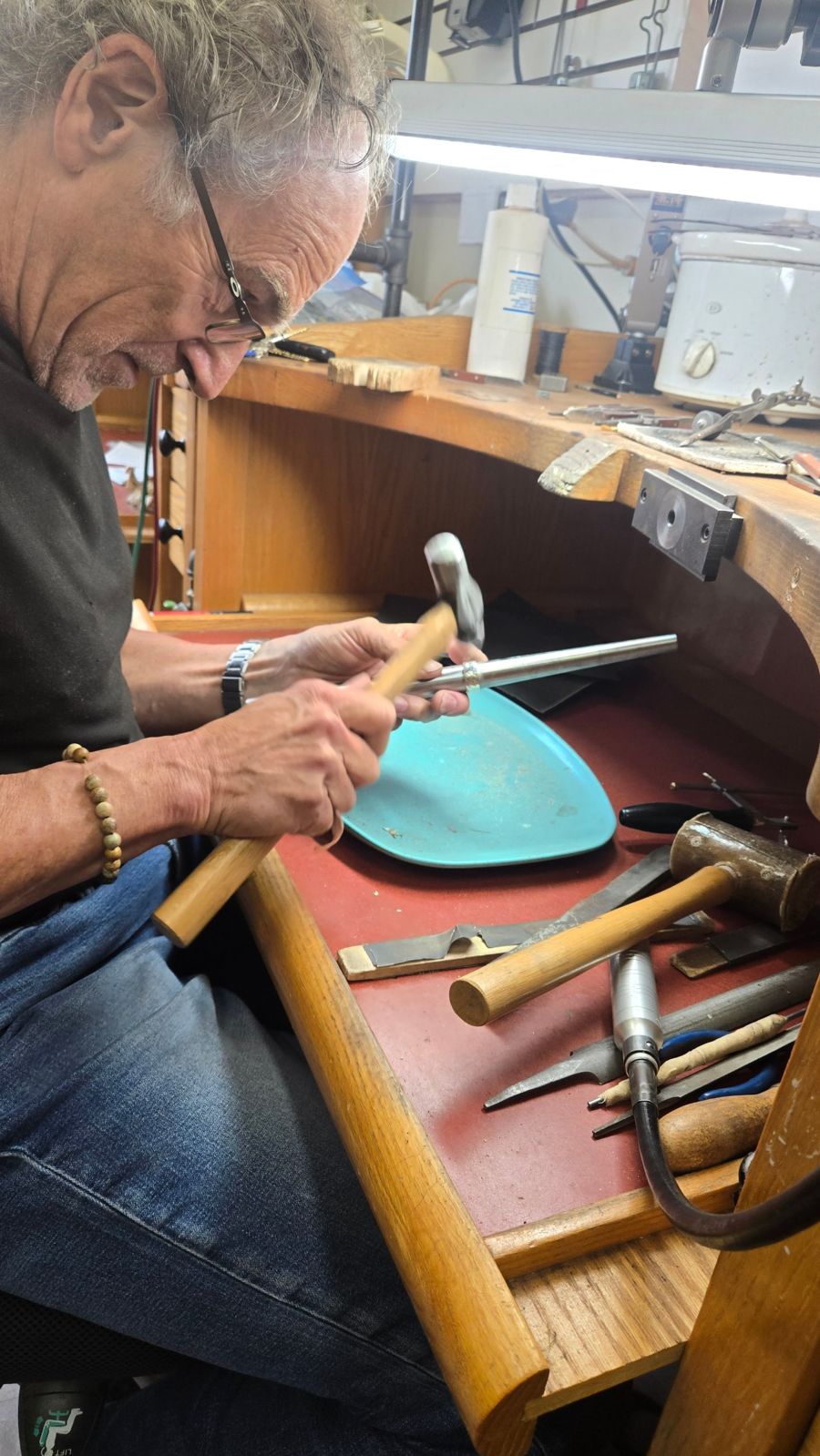 A Vernon Lapidary and Mineral Club member hammering a metal cuff at a jeweler's bench