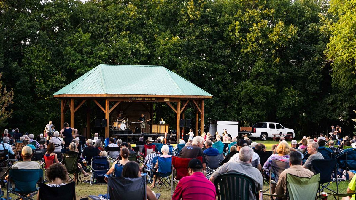 A crowd in lawn chairs watches a band play at the Lions Gazebo in Memorial Park, Armstrong, BC