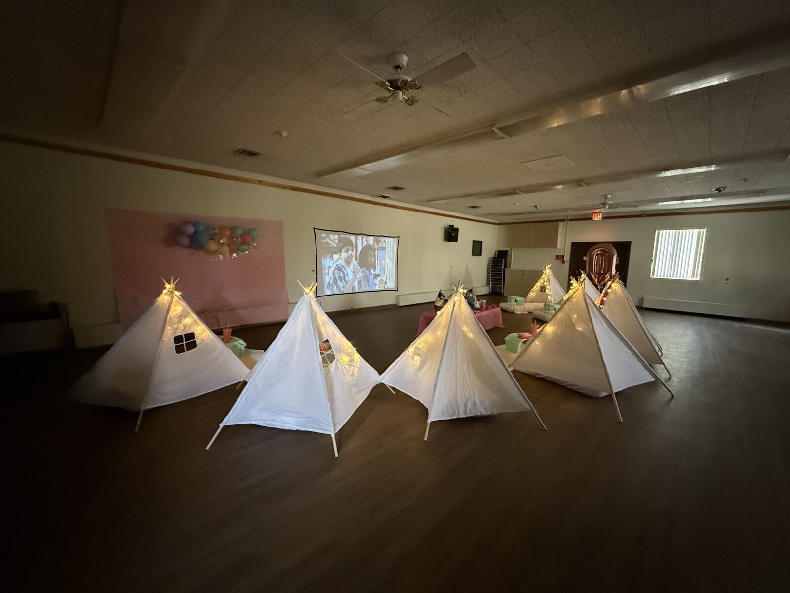 Lit white teepees set up across the wood floor of the main hall