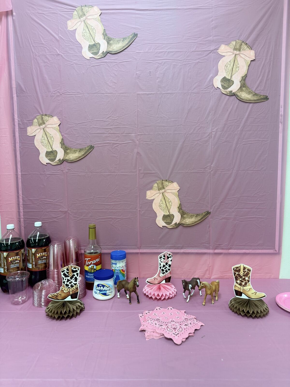 A pink cowgirl-themed treat table with boot decorations and horse figures