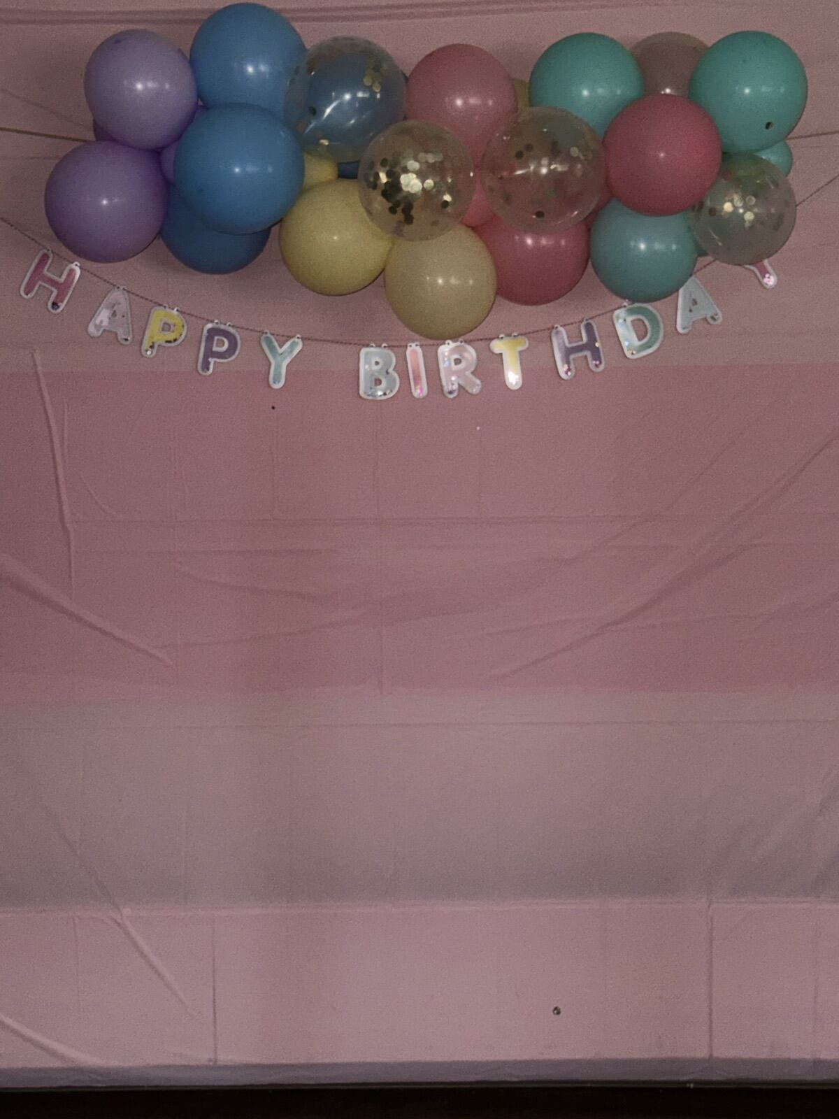 A pastel balloon garland and Happy Birthday banner over a pink backdrop